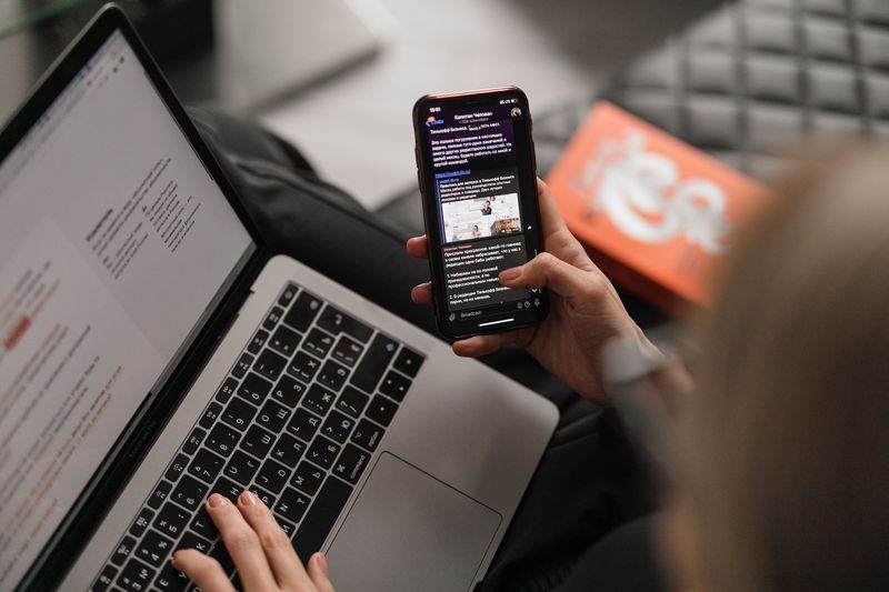 Person holding a phone next to a laptop